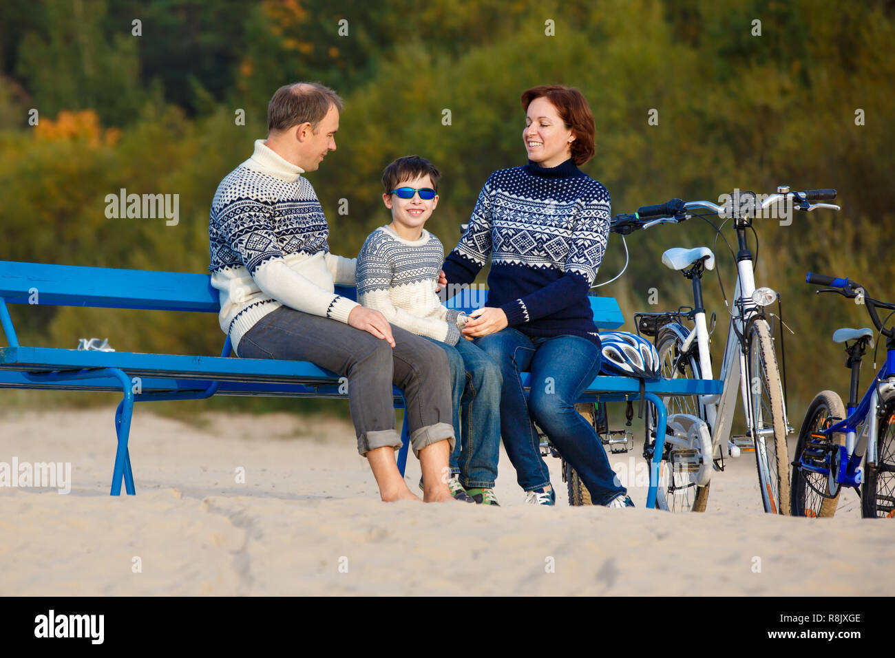 Young family of three having rest on bench during their bike riding on beach Stock Photo