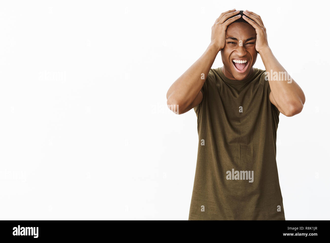 Portrait of pressured and intense fed up young african american male student yelling from distress holding hands on head in panic and losing temper, standing unhappy upset over gray background Stock Photo
