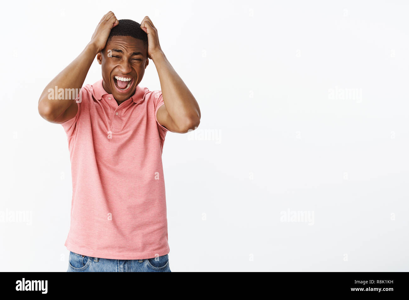 Sad displeased and annoyed african american young guy losing temper feeling fed up of lies pulling hair out of head in rafe and sorrow, yelling losing temper being displeased and sad standing in panic Stock Photo