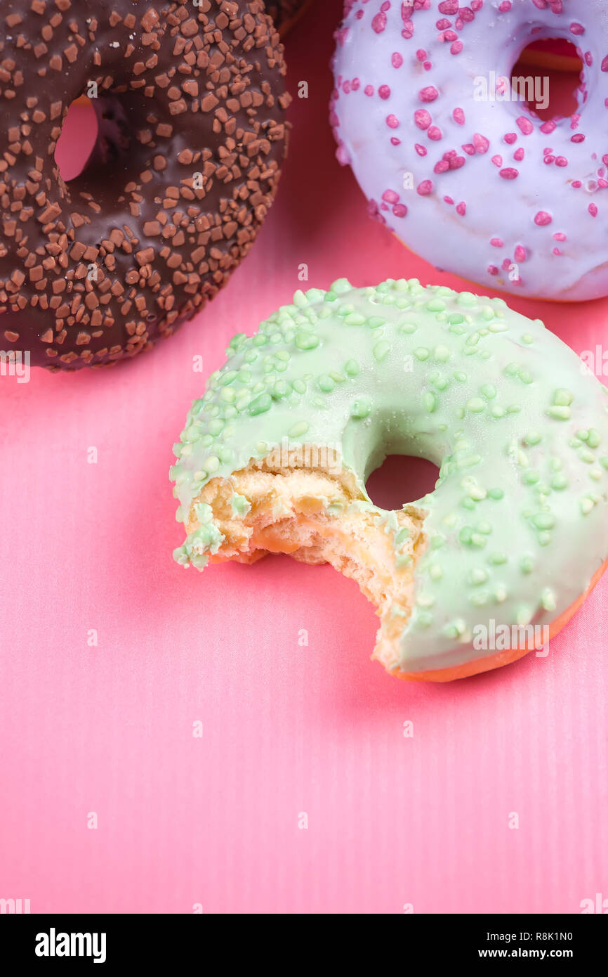 Sweet colorful tasty donuts with icing and sprinkles on pastel pink ...