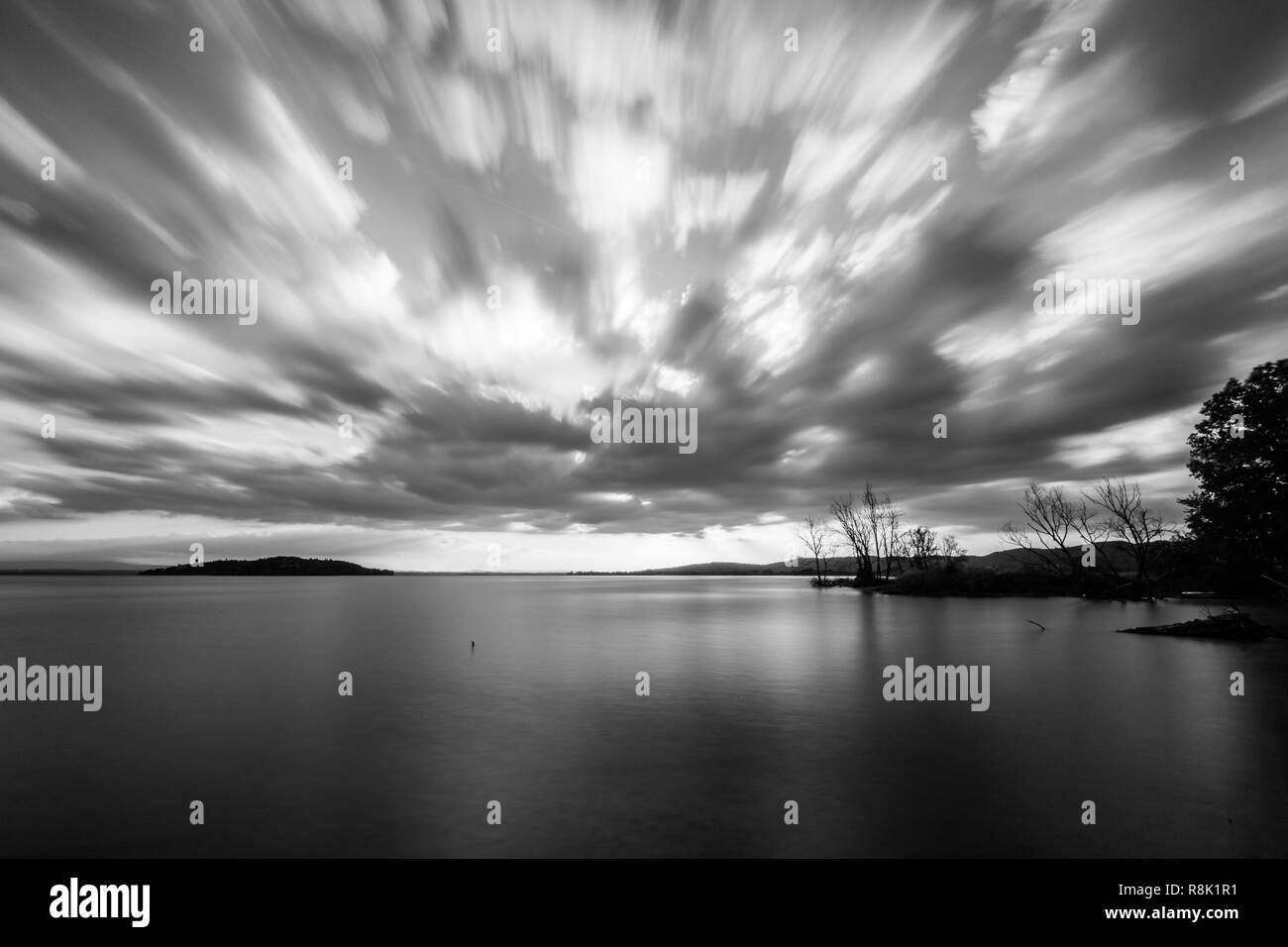 Beautiful wide angle view of a lake with an huge sky with clouds, above skeletal trees Stock Photo
