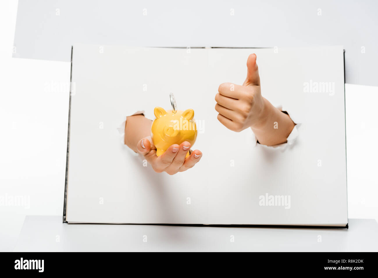 cropped shot of woman holding piggy bank with coin and showing thumb up ...