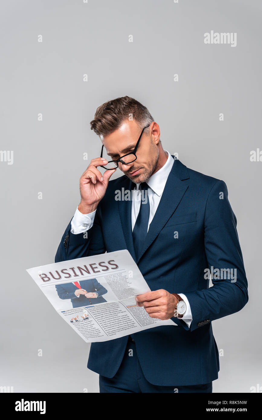handsome businessman touching glasses and reading newspaper isolated on ...