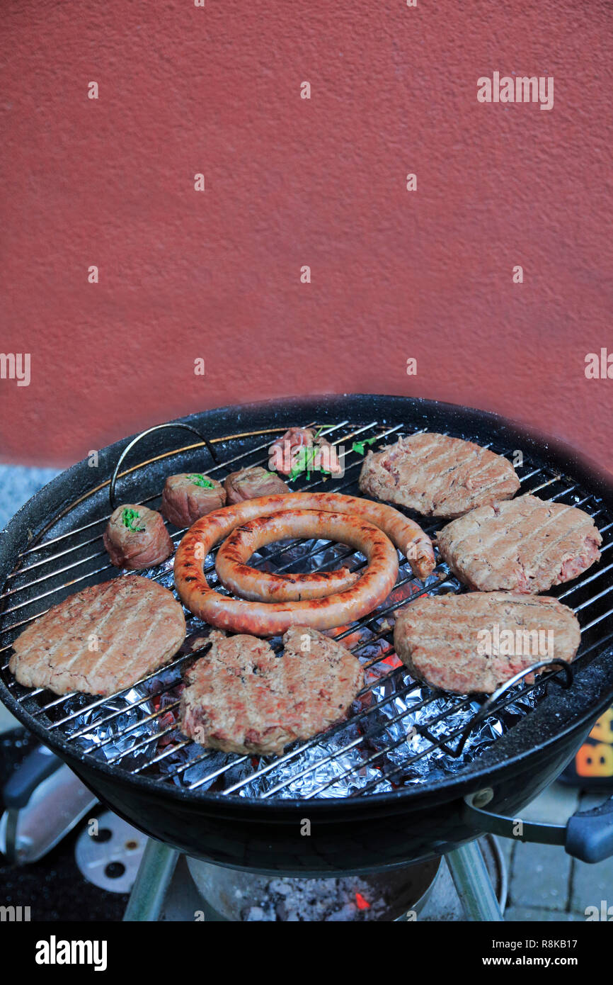 Paddies, Burger, Wurst und Fleischröllchen auf dem Holzkohle Grill Stock Photo