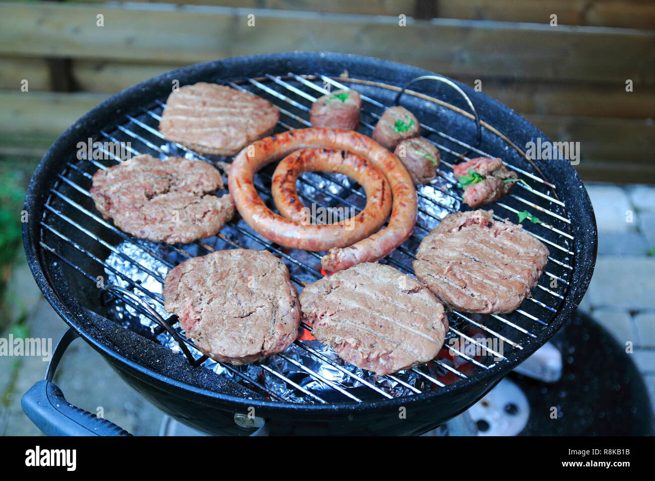 Paddies, Burger, Wurst und Fleischröllchen auf dem Holzkohle Grill Stock Photo