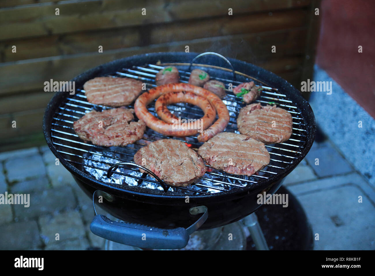 Paddies, Burger, Wurst und Fleischröllchen auf dem Holzkohle Grill Stock Photo