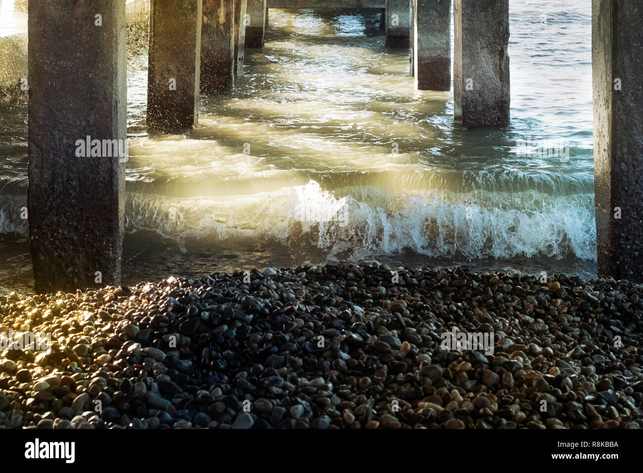 Concrete columns of a pier during a storm with a big wave in sunny day Stock Photo