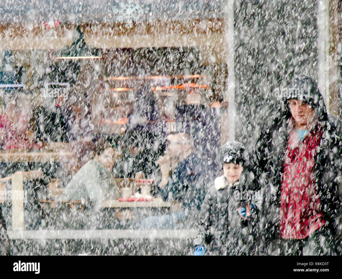Belgrade, Serbia - December 15, 2018: Father and son crossing he street in heavy snowfall and a young couple sitting in a restaurant behind them Stock Photo