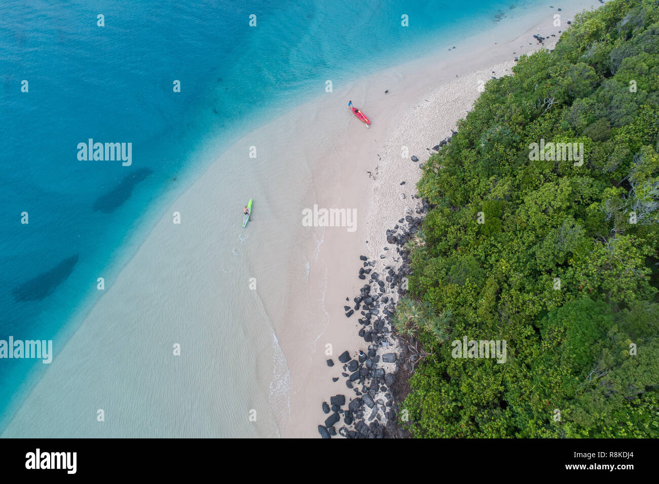 Man kayaking in a blue ocean near a tropical beach perfect for fitness, fun, fishing and holidays. Aerial shot at sunrise. Stock Photo