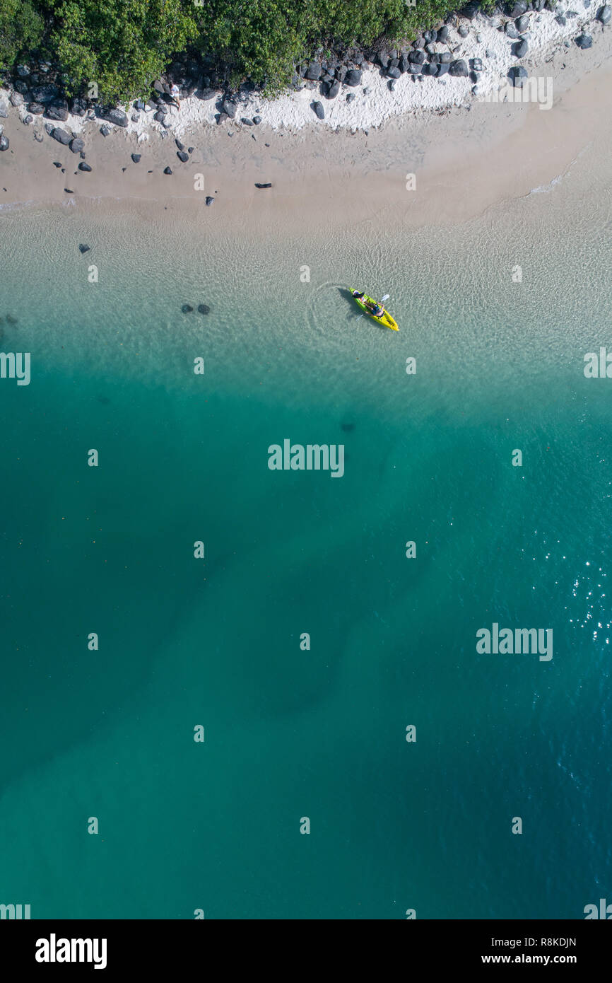 Man kayaking in a blue ocean near a tropical beach perfect for fitness, fun, fishing and holidays. Aerial shot at sunrise. Stock Photo