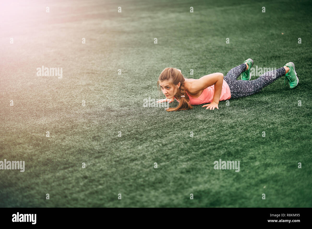 Fit woman in bright sports clothes to do burpees on the green grass Stock Photo