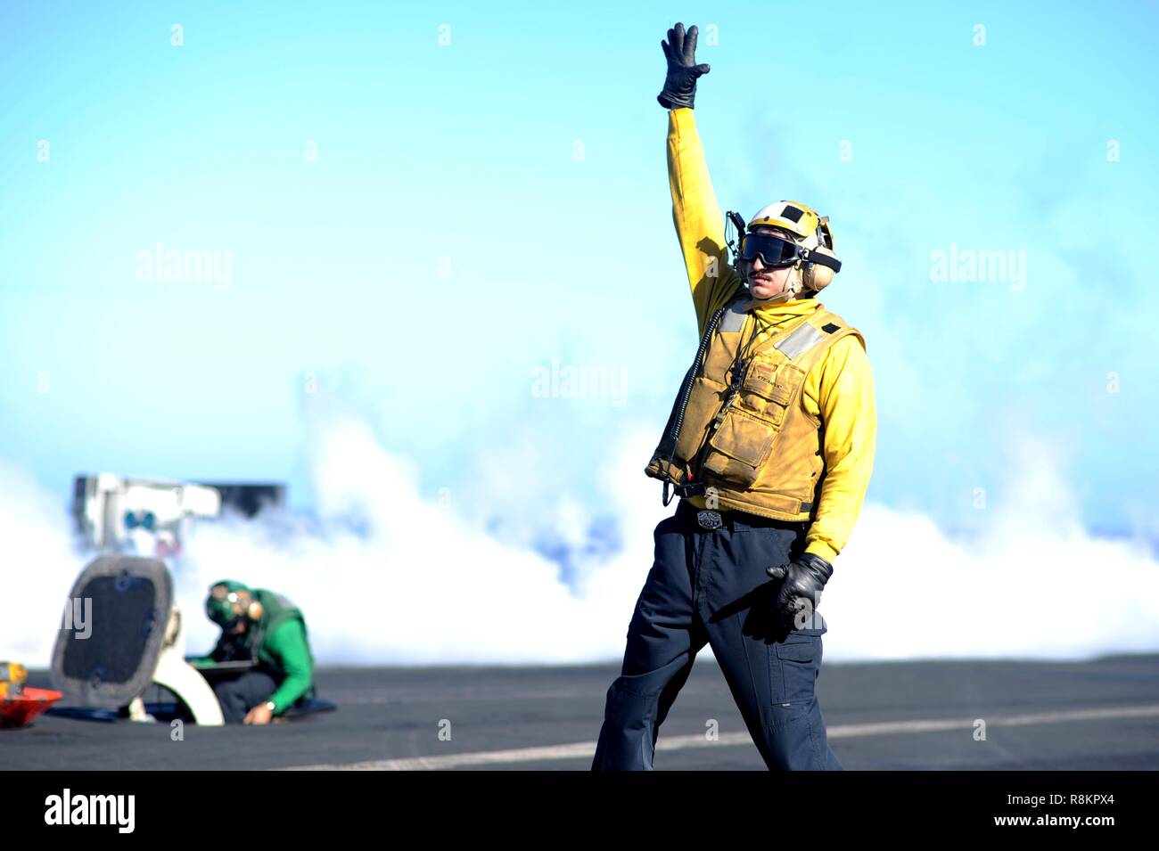An Aircraft Handler in a yellow shirt, signals the launch of a F/A-18 Super Hornet fighter aboard the Nimitz-class aircraft carrier USS Harry S. Truman December 7, 2018 in the Atlantic Ocean. Yellow shirts are worn by aircraft handlers, aircraft directors, Catapult Officers and Arresting Gear Officers considered the most difficult and important job on the flight deck. Stock Photo