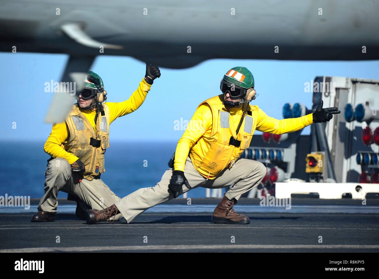 Flight directors known as yellow shirts, signal an F/A-18 Super Hornet to launch aboard the flight deck of the Nimitz-class aircraft carrier USS Harry S. Truman December 7, 2018 in the Atlantic Ocean. Yellow shirts are worn by aircraft handlers, aircraft directors, Catapult Officers and Arresting Gear Officers considered the most difficult and important job on the flight deck. Stock Photo