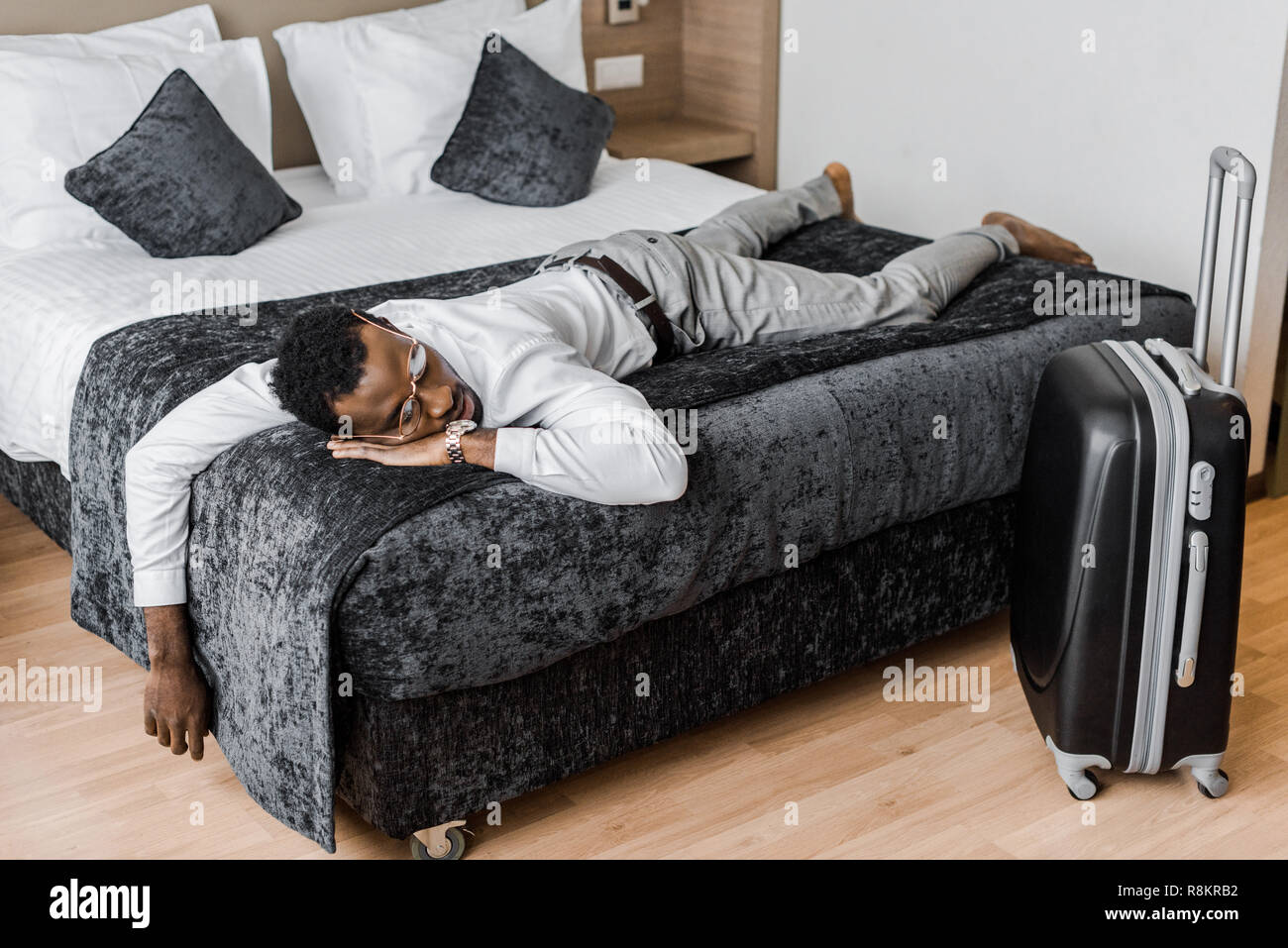tired african american man in formal wear sleeping on bed in hotel room  with suitcase Stock Photo - Alamy
