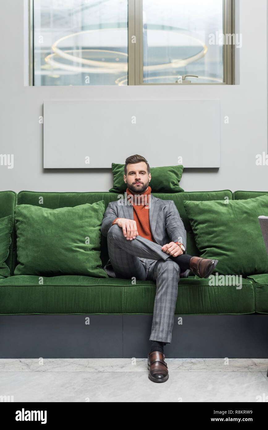 man in formal wear with legs crossed sitting on green sofa and looking at  camera Stock Photo - Alamy