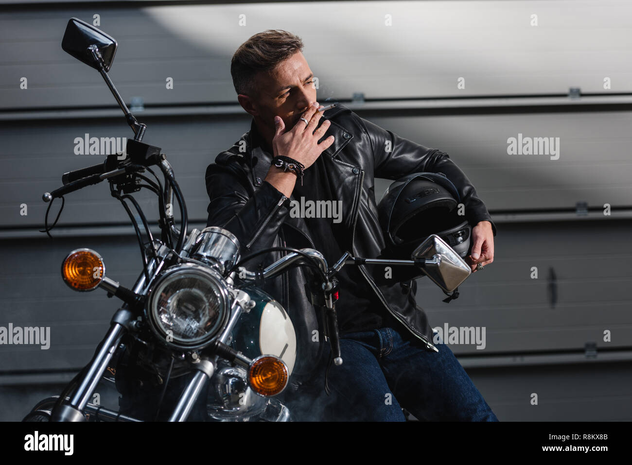handsome man smoking cigarette and holding motorbike helmet Stock Photo
