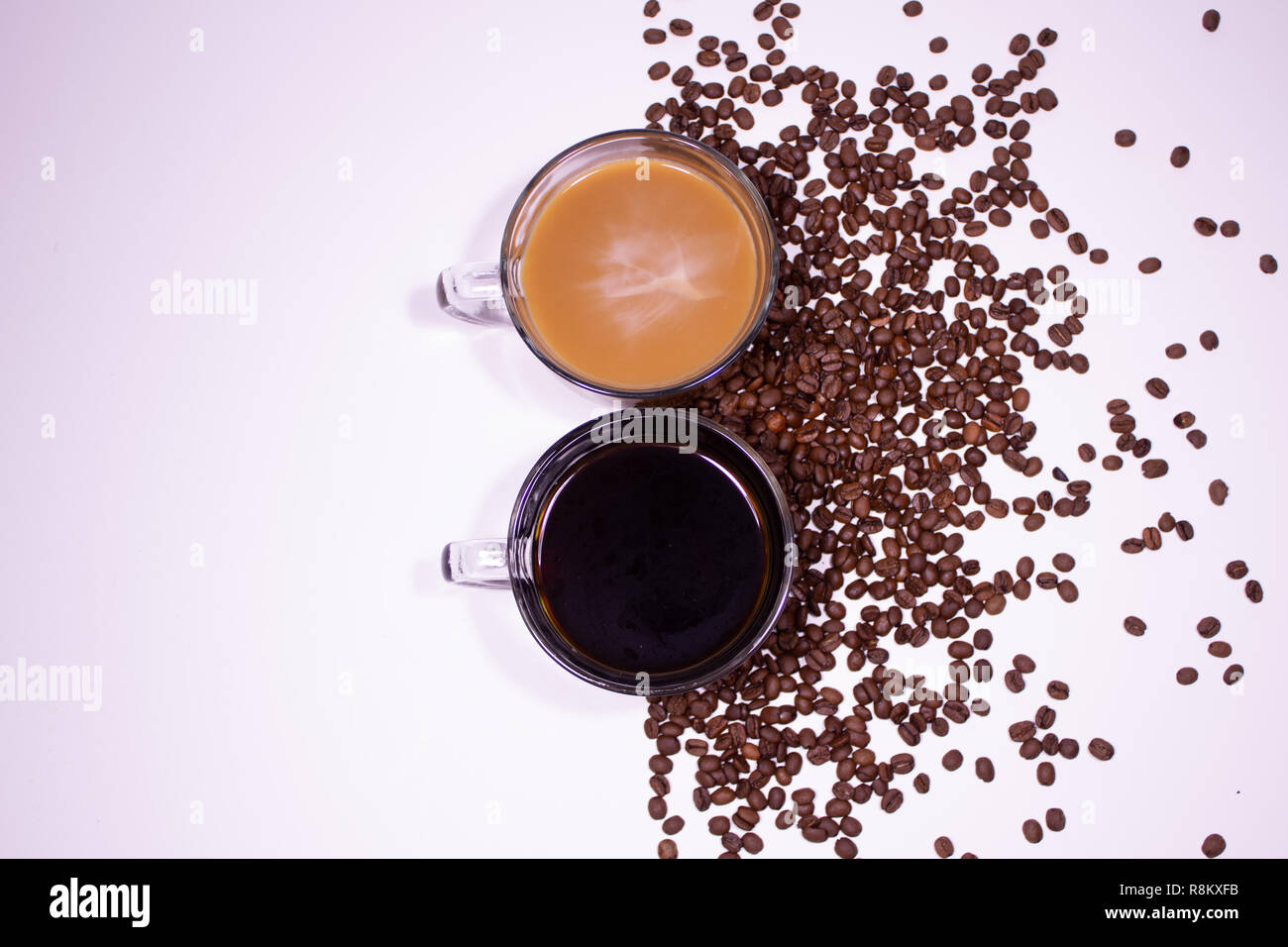 Two glass coffee mugs with coffee and cream on white table with coffee beans Stock Photo