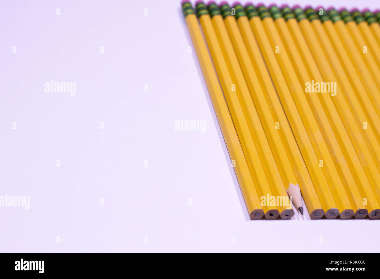 Dull pencils in a row with one sharpened pencil on a white table with