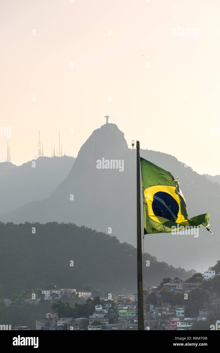 Brazilian flag waving as viewed from Forte Duque de Caxias in Leme, Rio de Janeiro, Brazil. Favela Babilônia slum and Christ the Reedemer Stock Photo