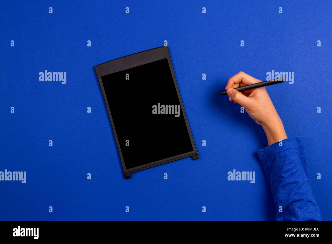 Kid hand with graphic tablet and stylus pen on blue background. Stock Photo
