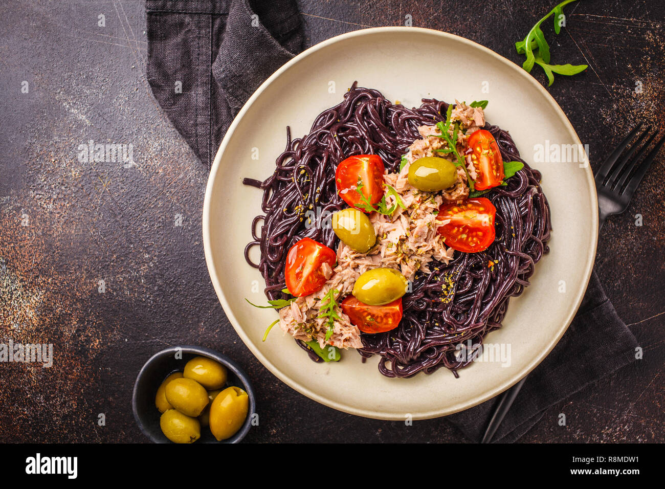 Black rice pasta with tuna, tomatoes and olives in a white plate, dark ...
