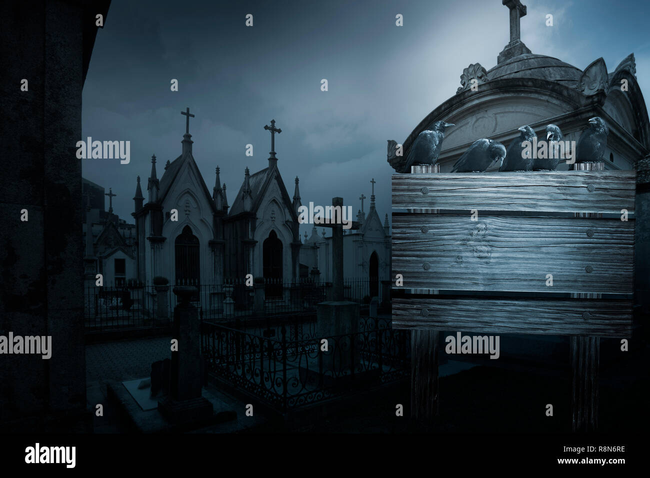 Spooky halloween background with crows, tombs in the form of chpel from an old european cemetery street and wooden placard in the foreground with spac Stock Photo
