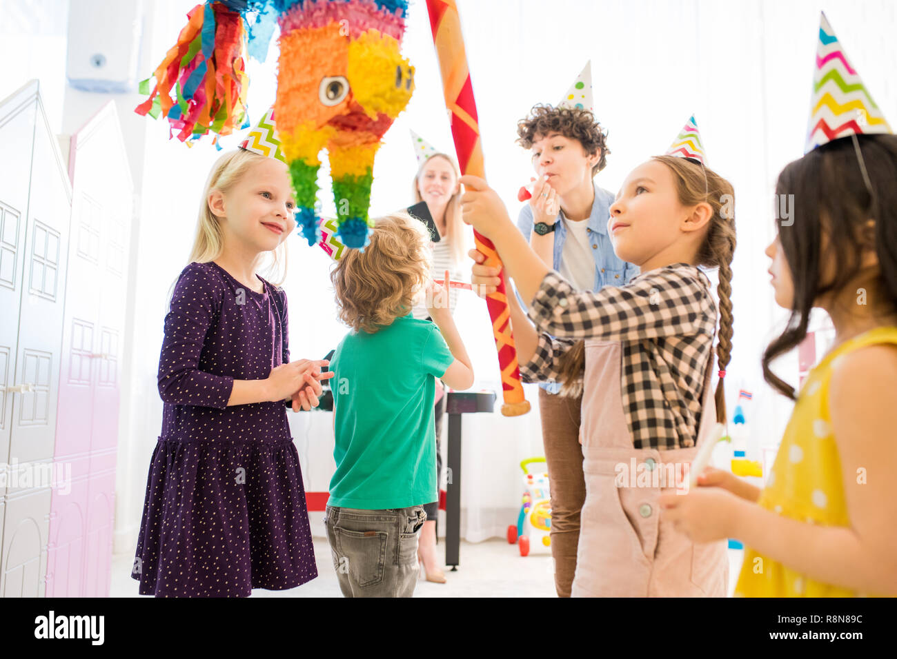 Confident girl hitting colorful pinata at kids celebration Stock Photo