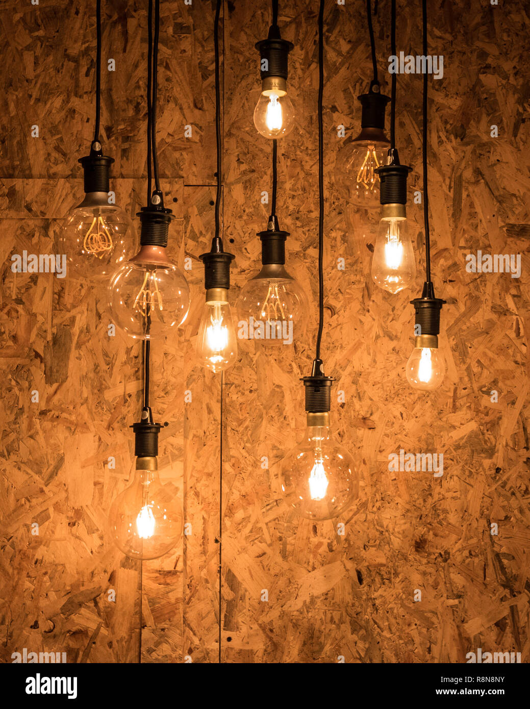 Multiple light bulbs hanging from ceiling against a wooden background Stock  Photo - Alamy