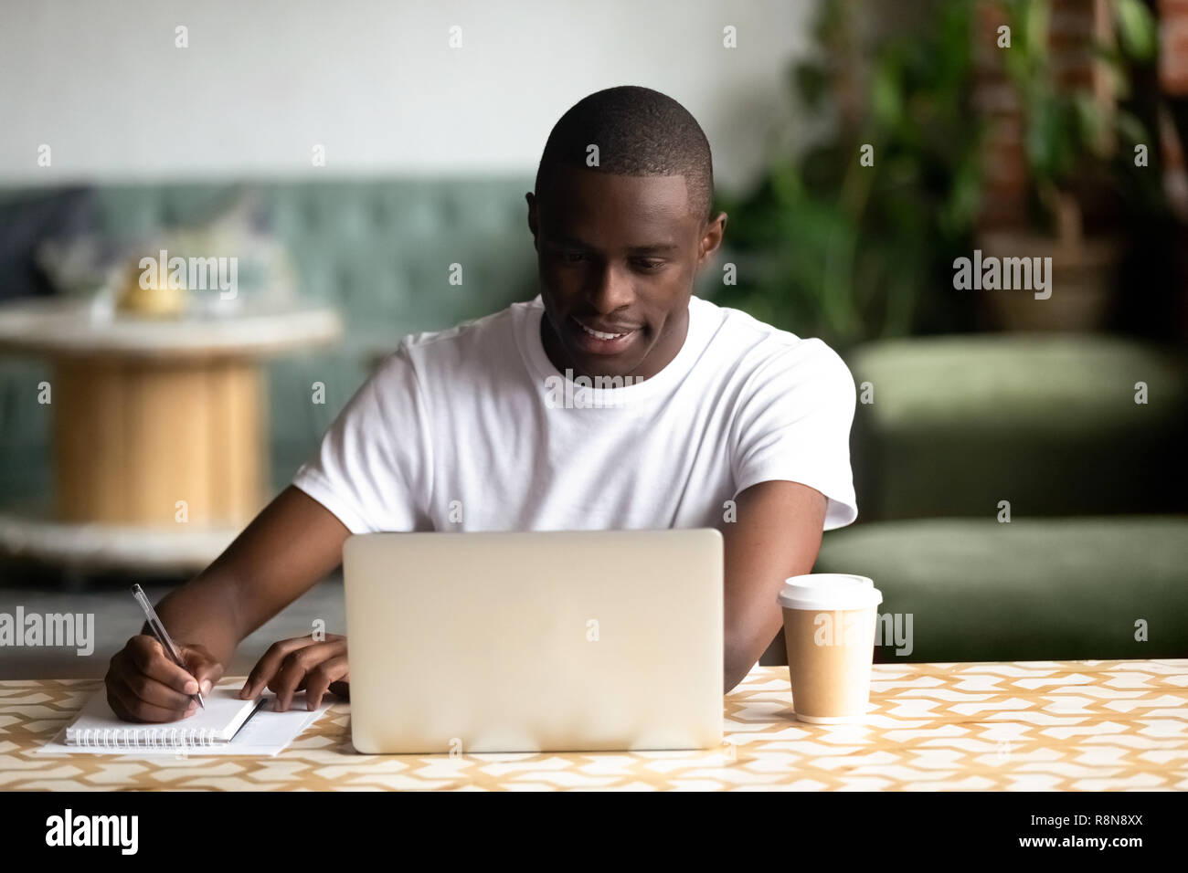 Smiling African American man using laptop, making notes Stock Photo