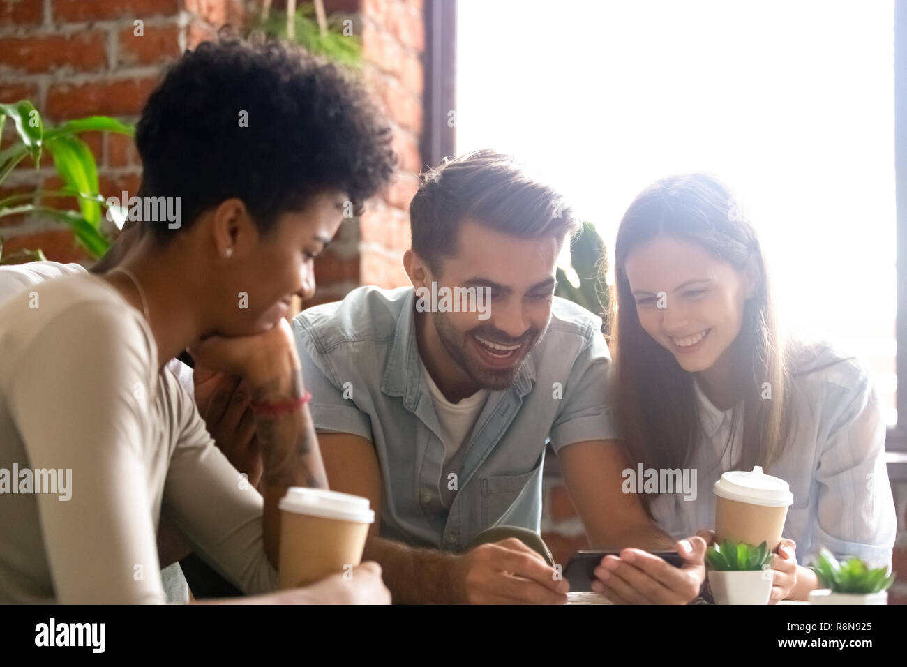 Happy diverse friends using phone together in cafe Stock Photo