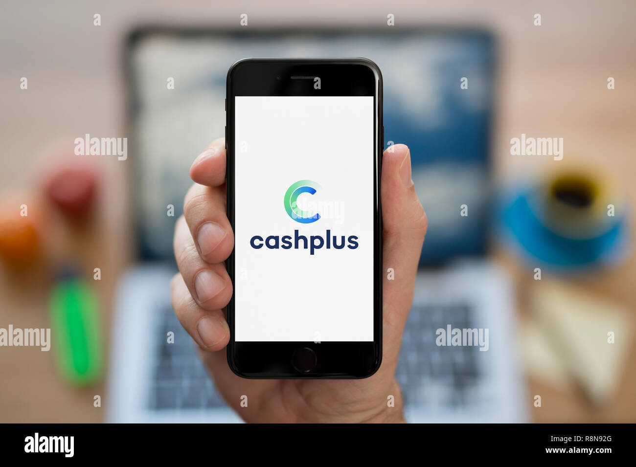 A man looks at his iPhone which displays the CashPlus logo (Editorial use only). Stock Photo