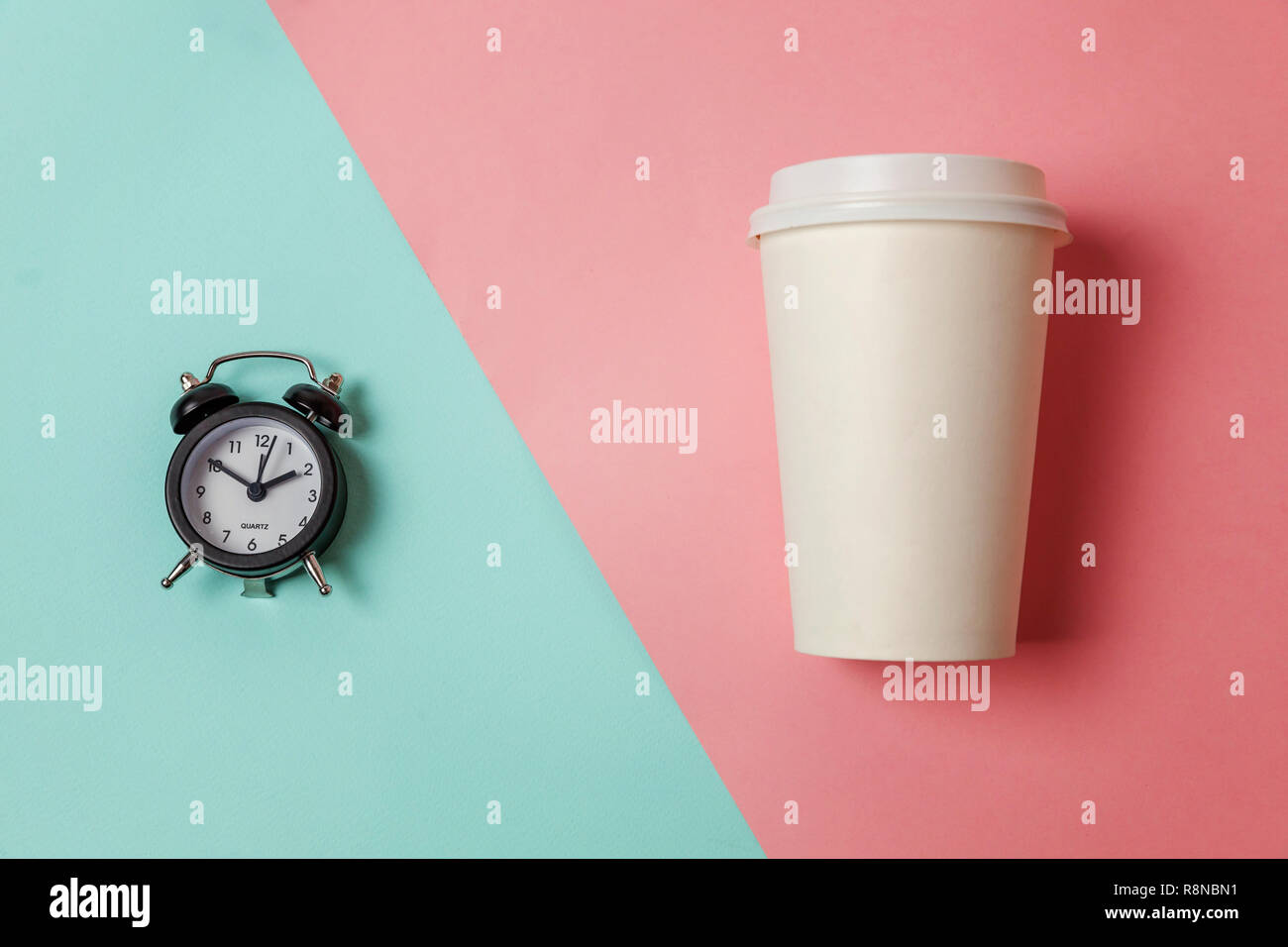 Simply flat lay design paper coffee cup and alarm clock on blue pink pastel colorful trendy background. Takeaway drink and breakfast beverage. Good mo Stock Photo