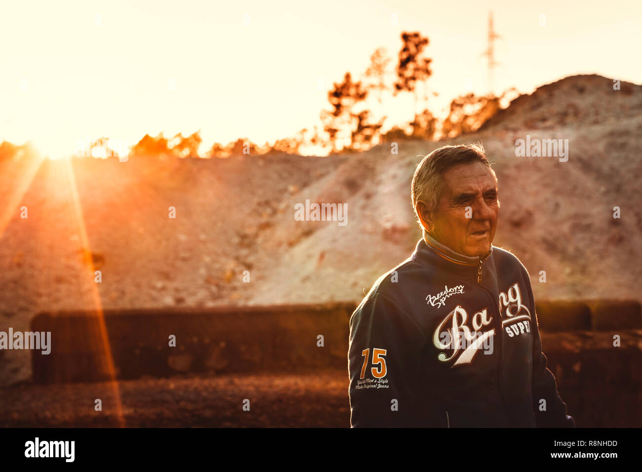 Handsome senior man posing standing with the sun flare on his back at sunset Stock Photo