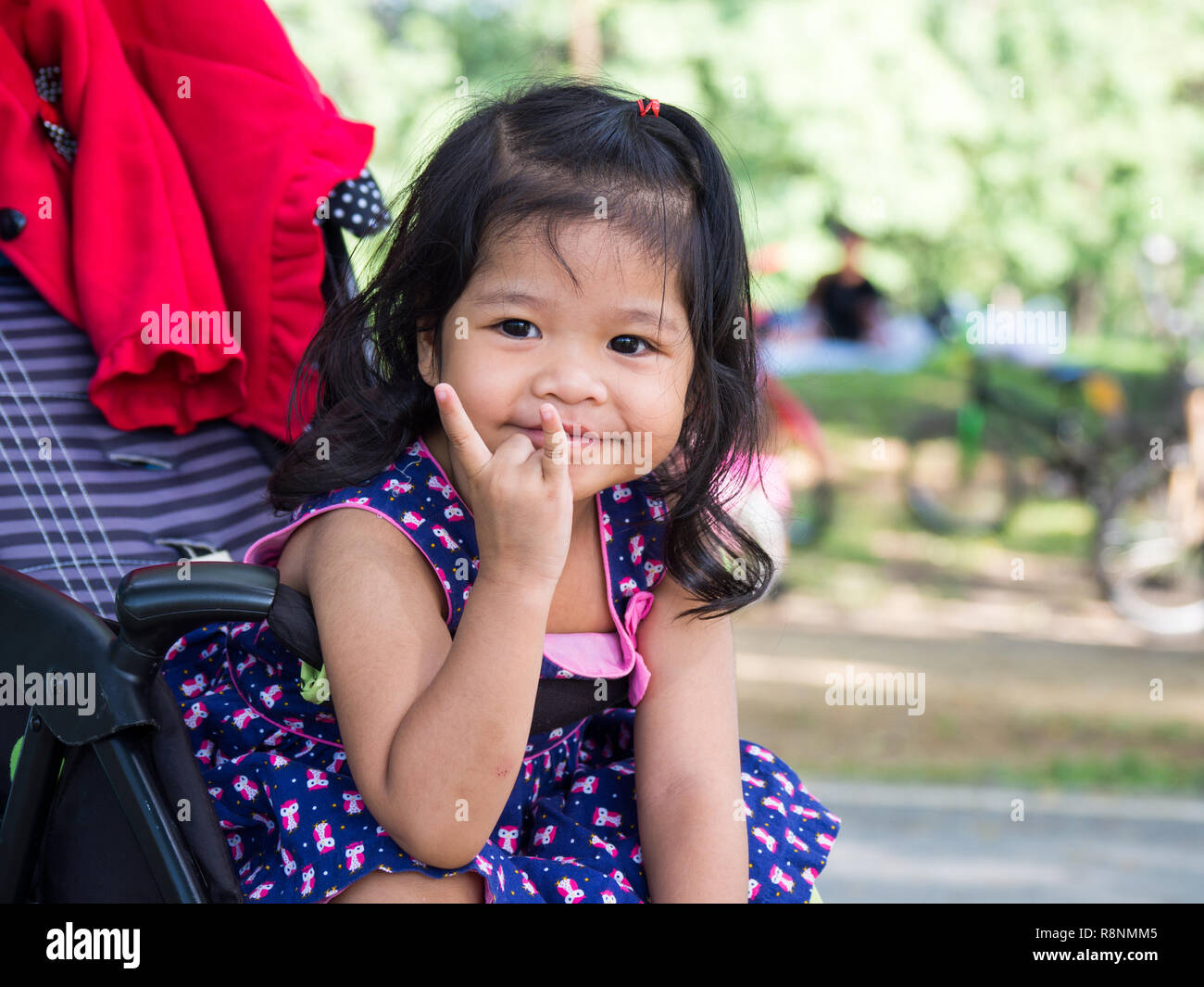 Little asian girl sitting in a stroller at public park. She have be ...