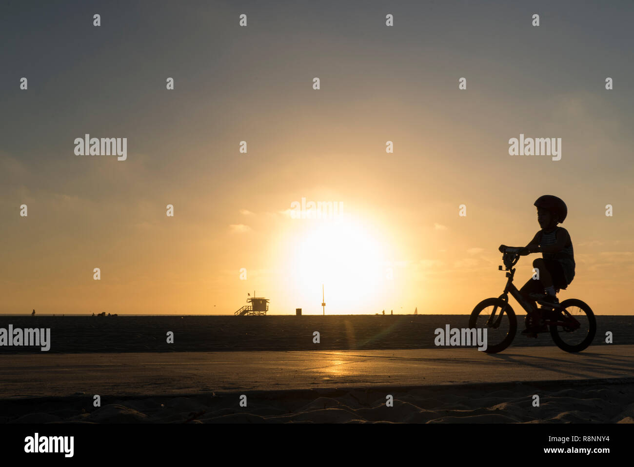boy backlit by the sunset rides his bicycle at the beach Stock Photo