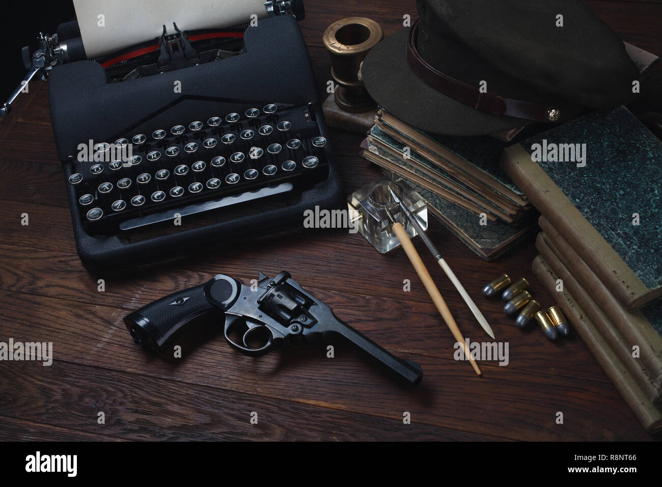 Writing a detective story - old retro vintage typewriter and revolver gun with ammunitions, books, papers, old ink pen on wooden table Stock Photo