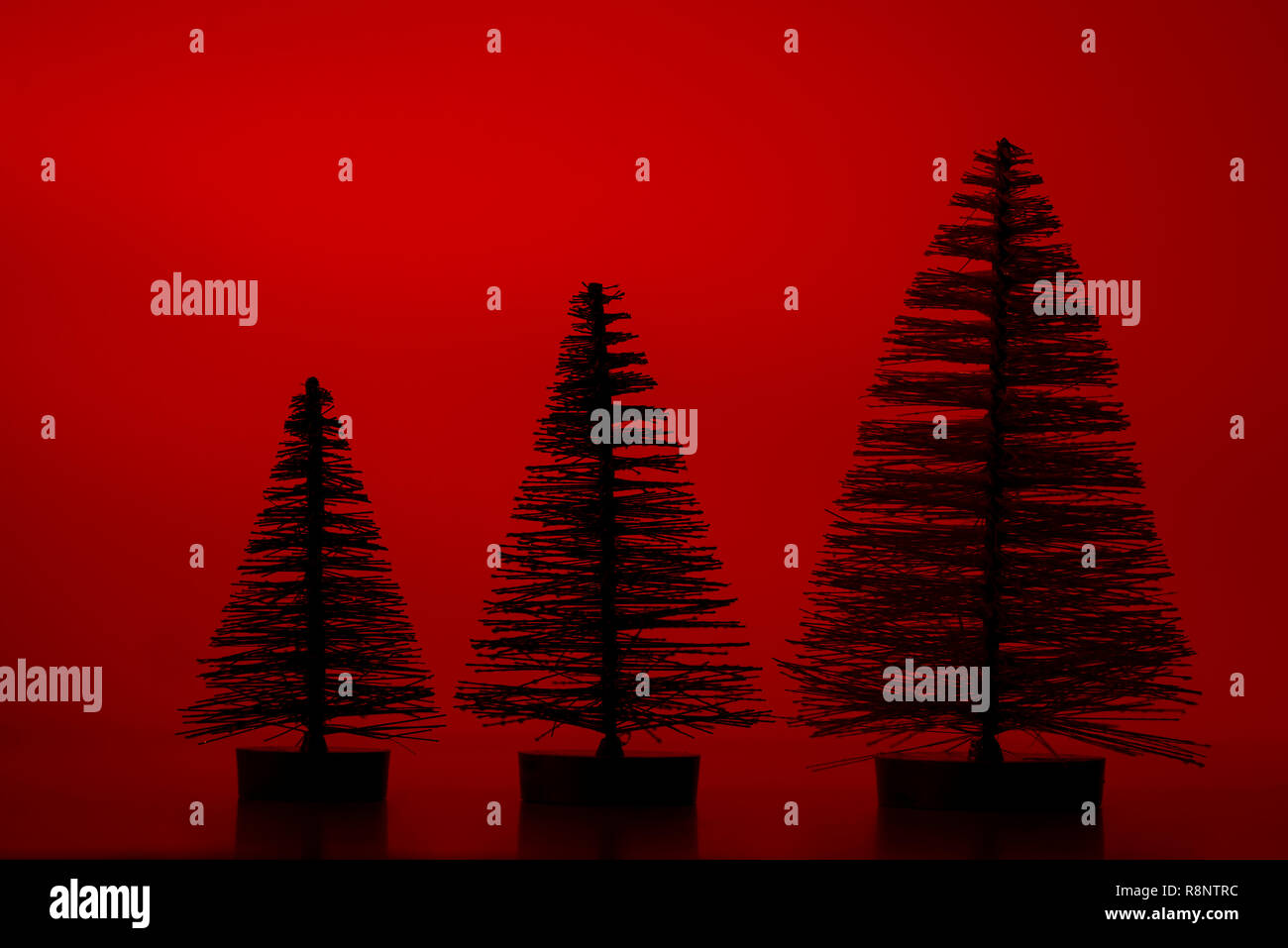 Three silhouette artificial pine trees on a red background Stock Photo ...