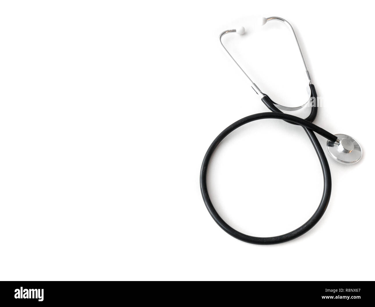 A doctors black flexible rubber and steel metal heart pulse stethoscope laying isolated on a white table top. Stock Photo