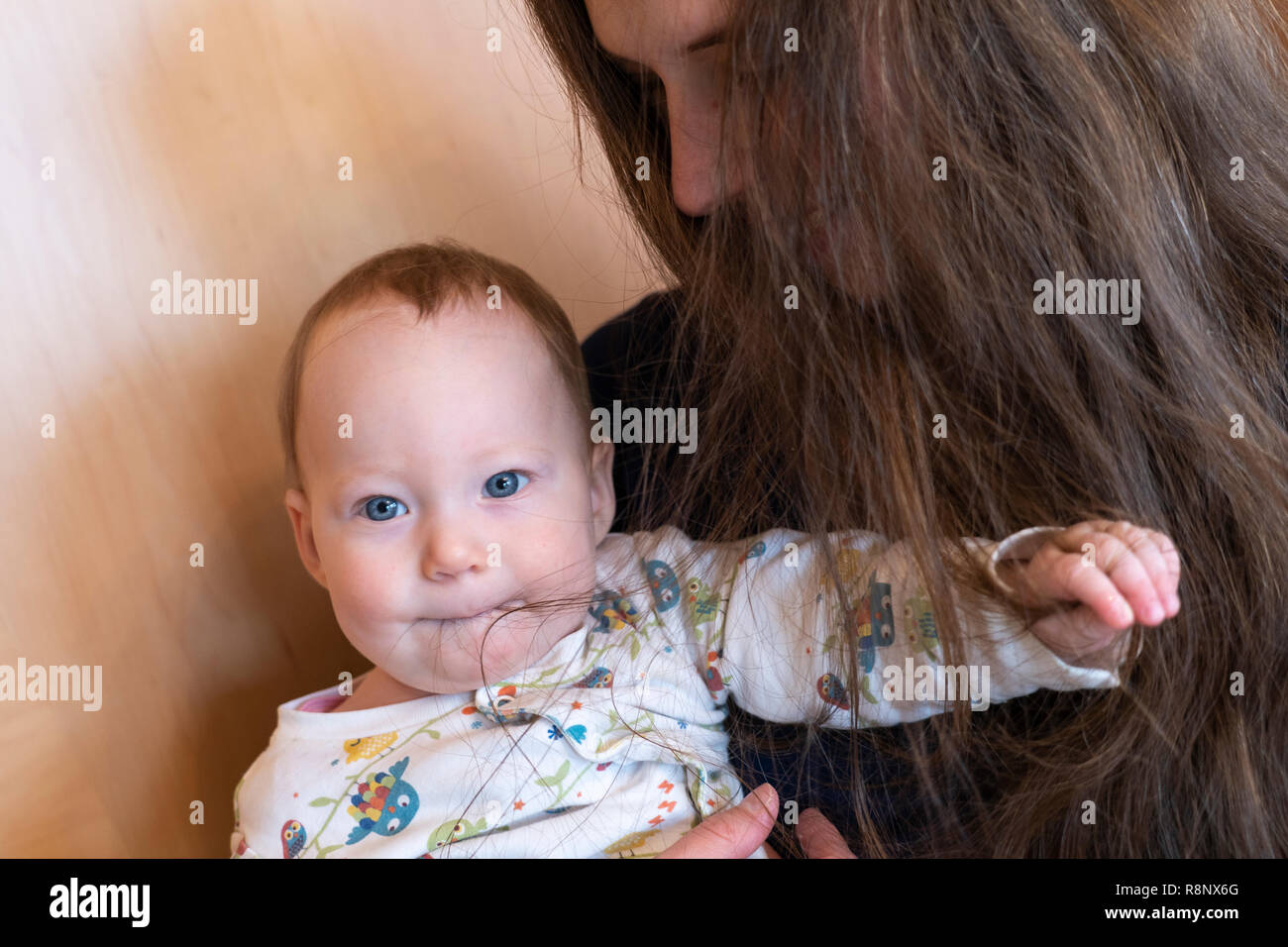 A baby girl being held by her mother and playing with her mother's hair Stock Photo