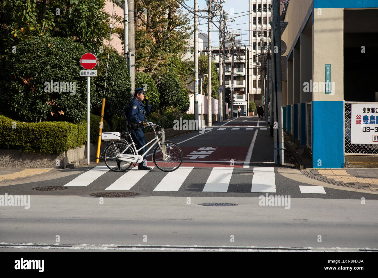A Japanese policeman with bicycle walking in the Ikebukuro area in Tokyo Stock Photo