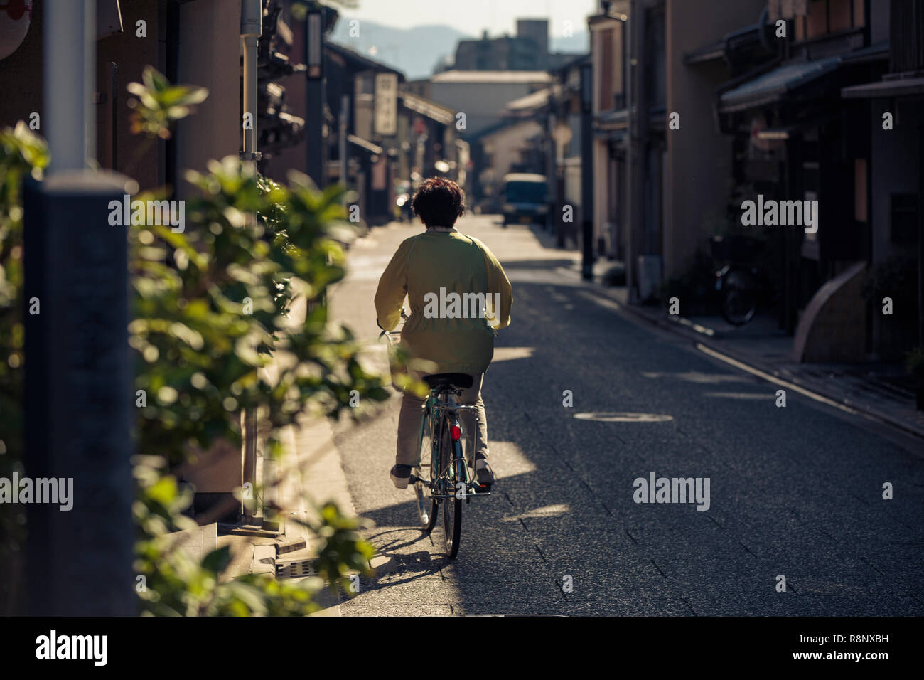 An elderly Japanese lady cycles down an elegant traditional street in Kyoto, Japan. Stock Photo