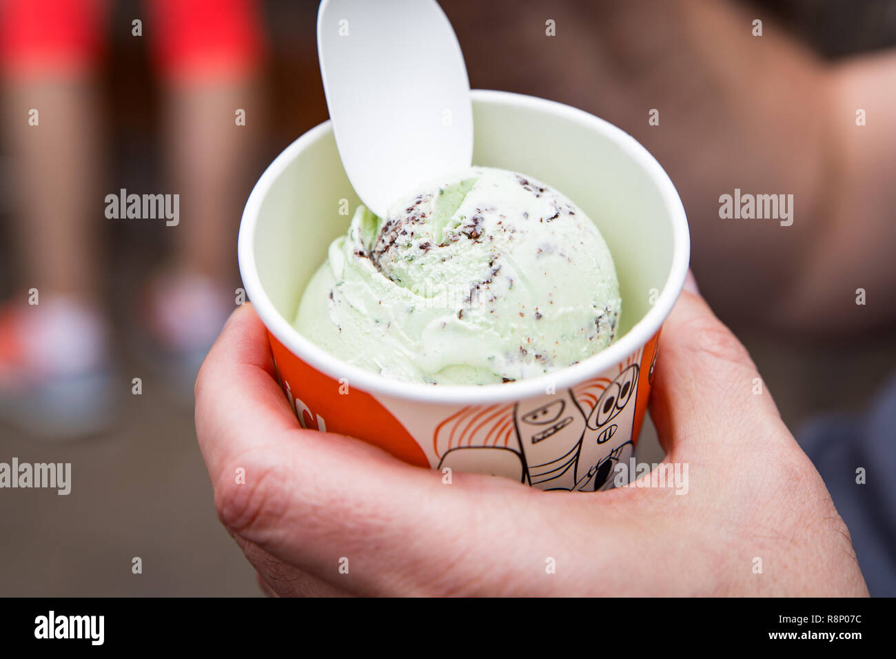 Enjoying a serving of mint and chocolate chip gelato served in a tub with a plastic spoon Stock Photo