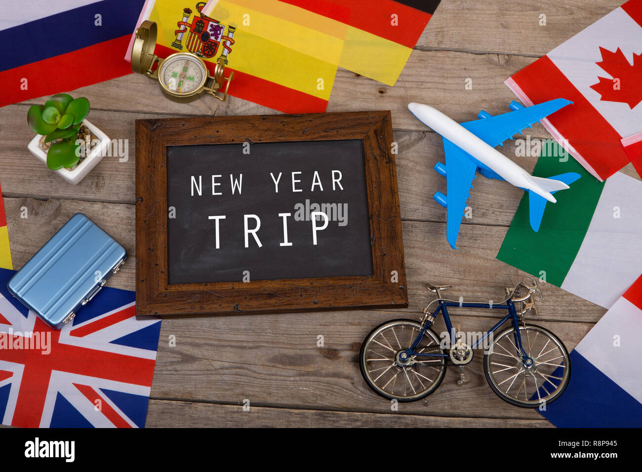 Travel time - blackboard with text 'New Year trip', flags of different countries, airplane model, little bicycle and suitcase, compass on wooden backg Stock Photo