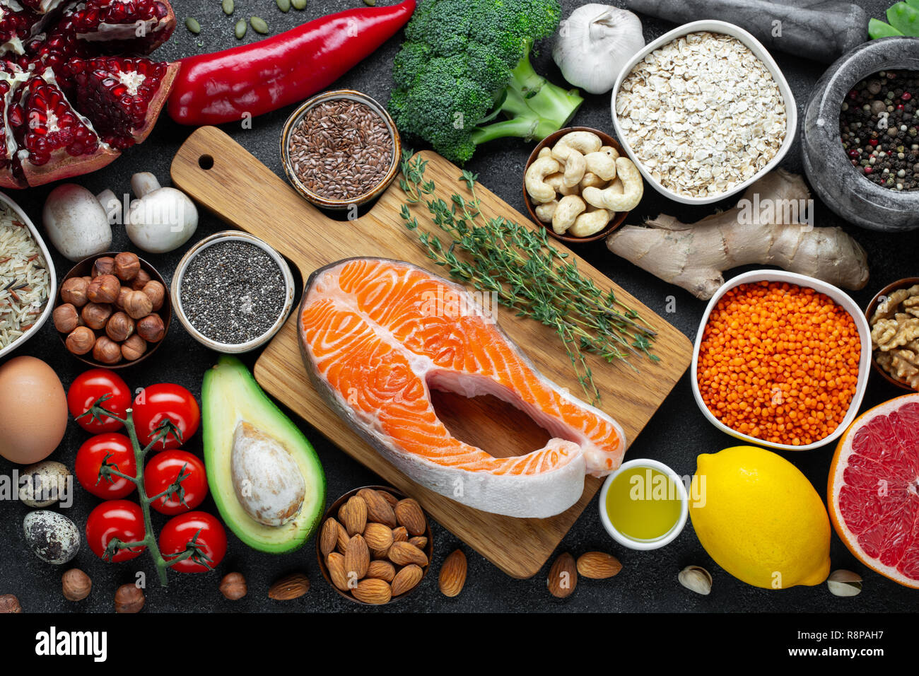 Healthy food clean eating selection: fish, fruit, nuts, vegetable, seeds, superfood, cereals, leaf vegetable on black concrete background. Flat lay Stock Photo