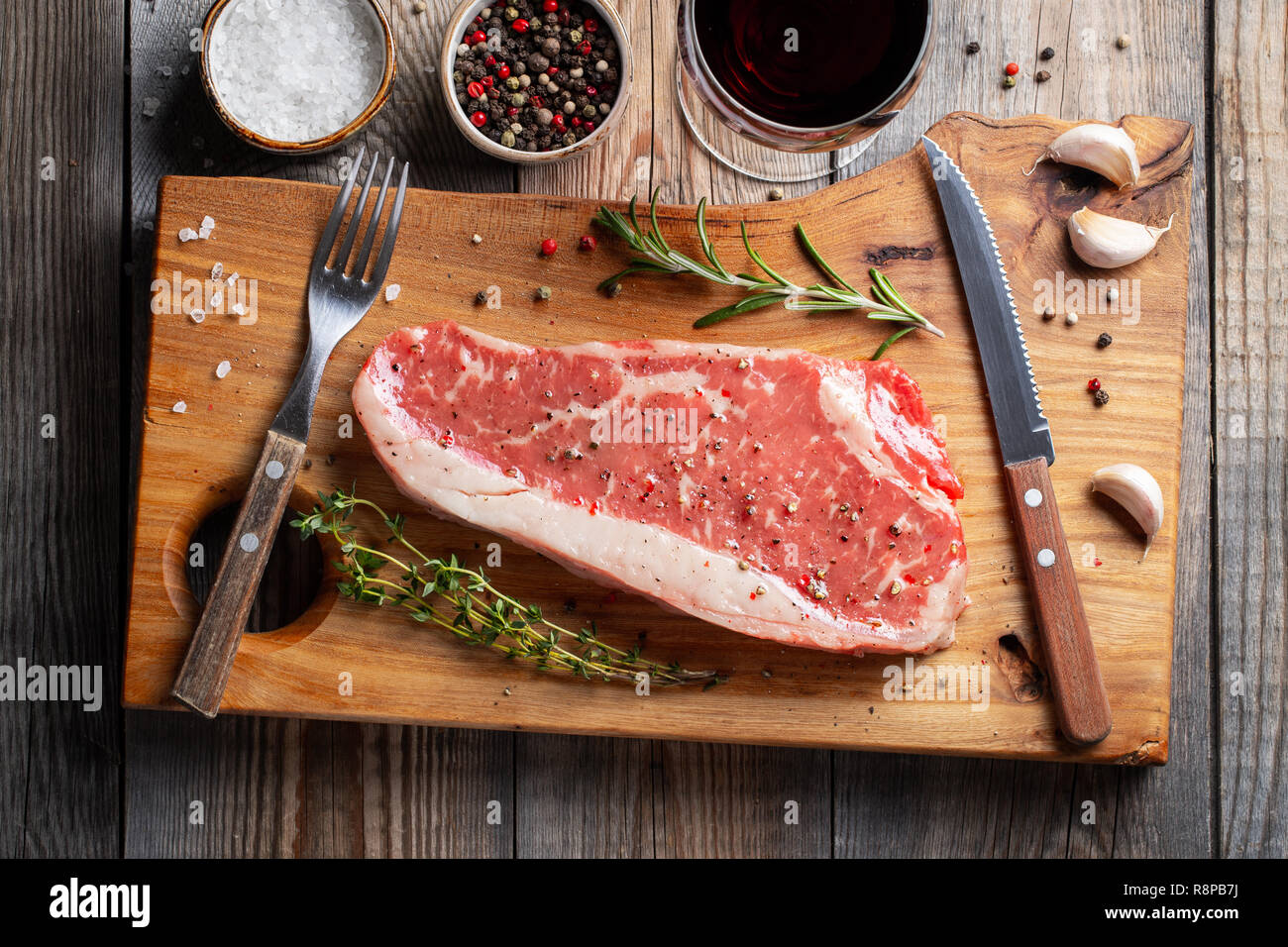 Fresh raw Prime Black Angus beef steaks with spices and red wine on wooden board: Striploin, Rib Eye. Top view. On a dark rustic table Stock Photo