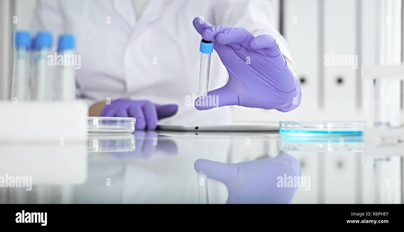 Close-up of professional female scientist in protective eyeglasses making experiment with reagents in laboratory or making blood tests. Medicine, science and research concept Stock Photo