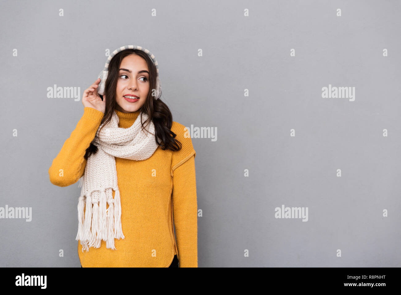 Portrait of beautiful woman wearing ear muffs and scarf looking aside isolated over gray background Stock Photo