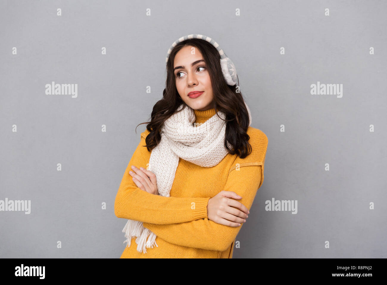 Portrait of attractive woman wearing ear muffs and scarf looking aside isolated over gray background Stock Photo