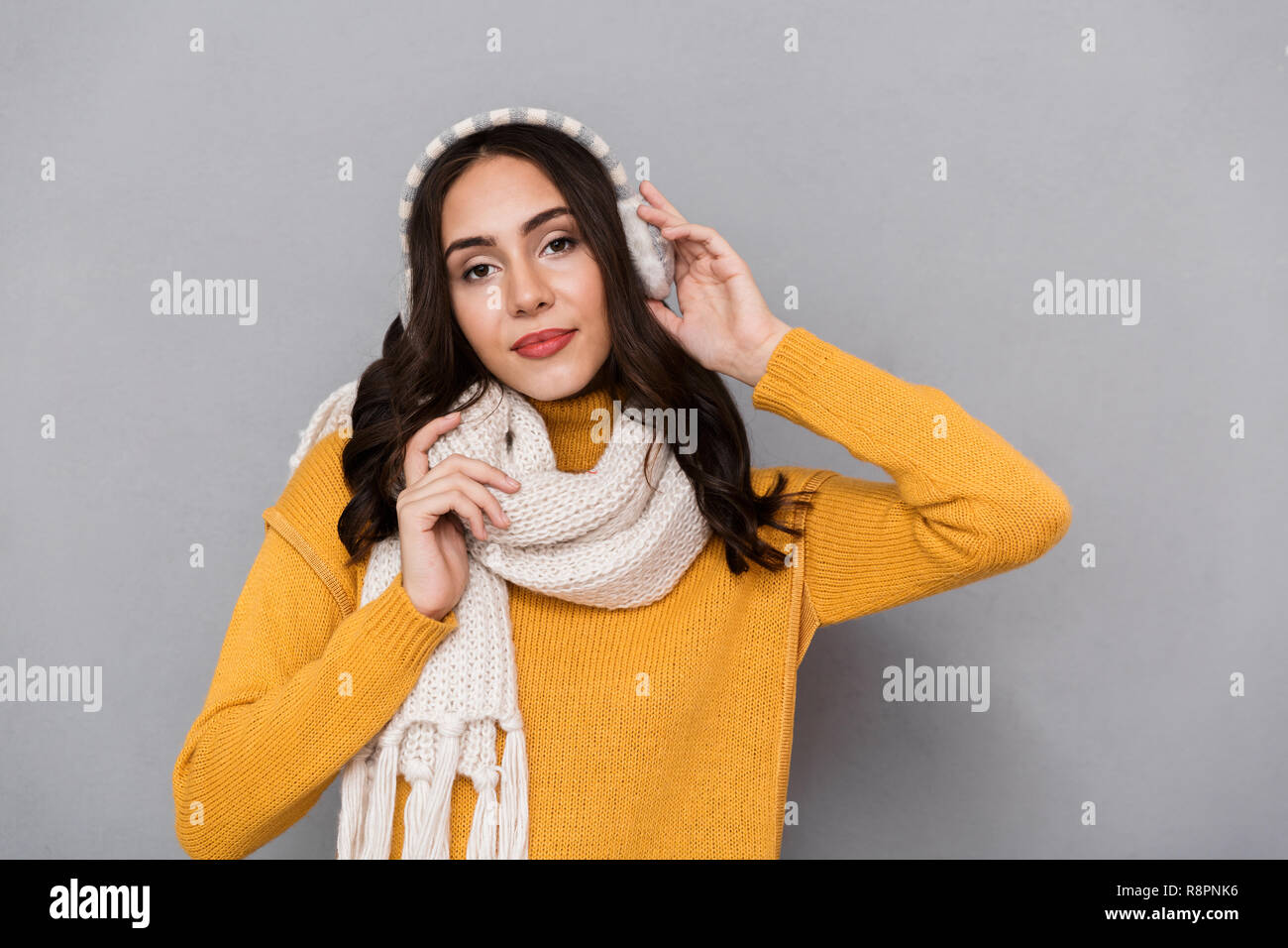 Portrait of adorable woman wearing ear muffs and scarf looking at camera isolated over gray background Stock Photo