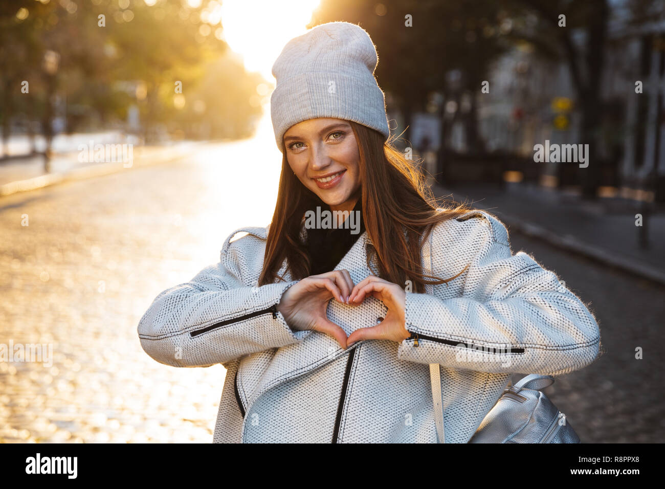 Cheerful young woman dressed in autumn coat and hat walking outdoors at the city street Stock Photo